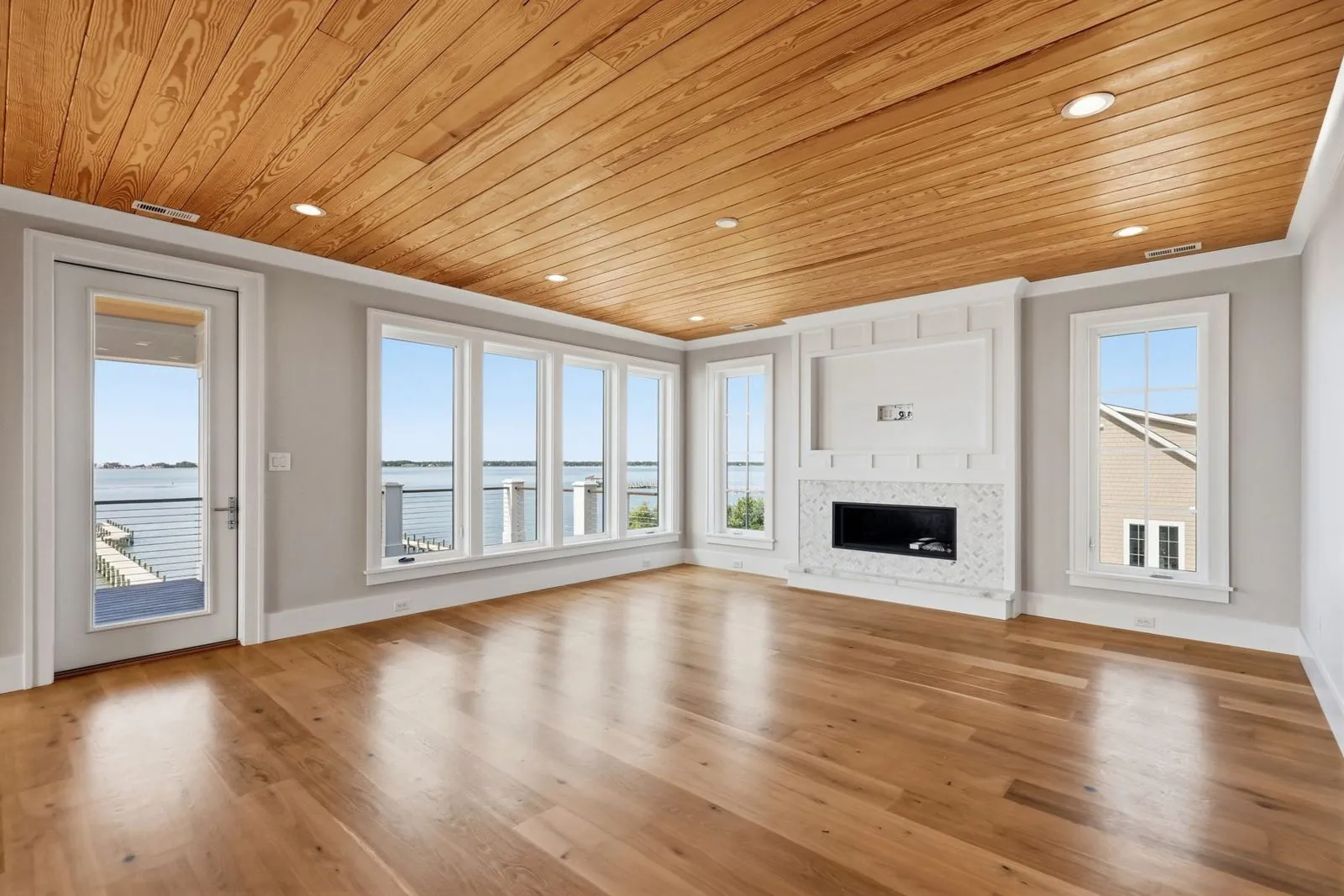 Great room with pine plank ceiling, linear gas fireplace and windows to the sound